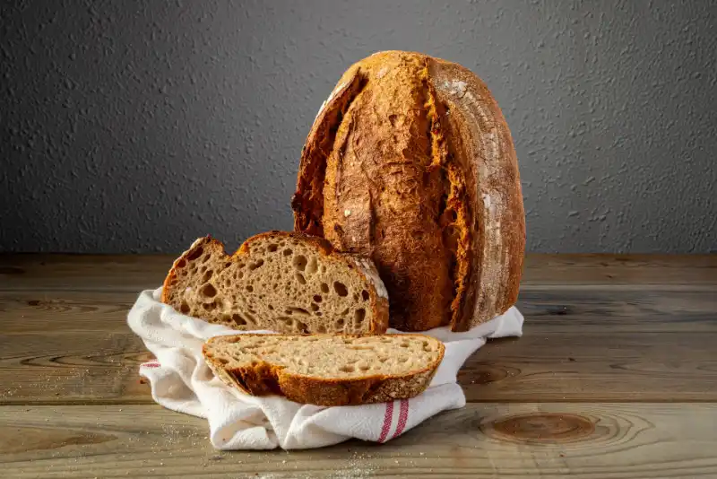 Pan artesanal especial colocado verticalmente, con dos hogazas del mismo pan sobre un paño blanco en primer plano.