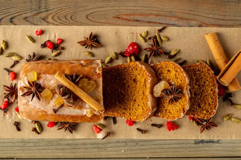 Plano cenital de una cake de calabaza especiada cortada en rebanadas sobre una mesa. A su alrededor hay decoración de diversas especias.